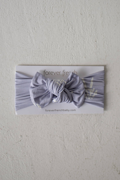 Forever French Baby Enchanted Skelly bamboo head wrap in lavender with a bow, shown on its packaging card