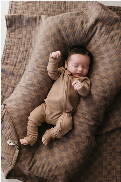 Newborn in a brown zip romper lying on the faded brown checkerboard muslin quilt