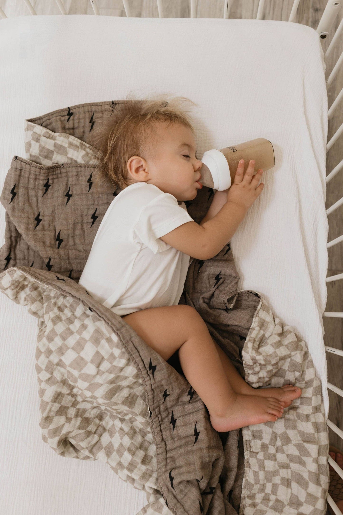 Baby napping in a crib alongside the lightning bolt and wavy checker muslin quilt