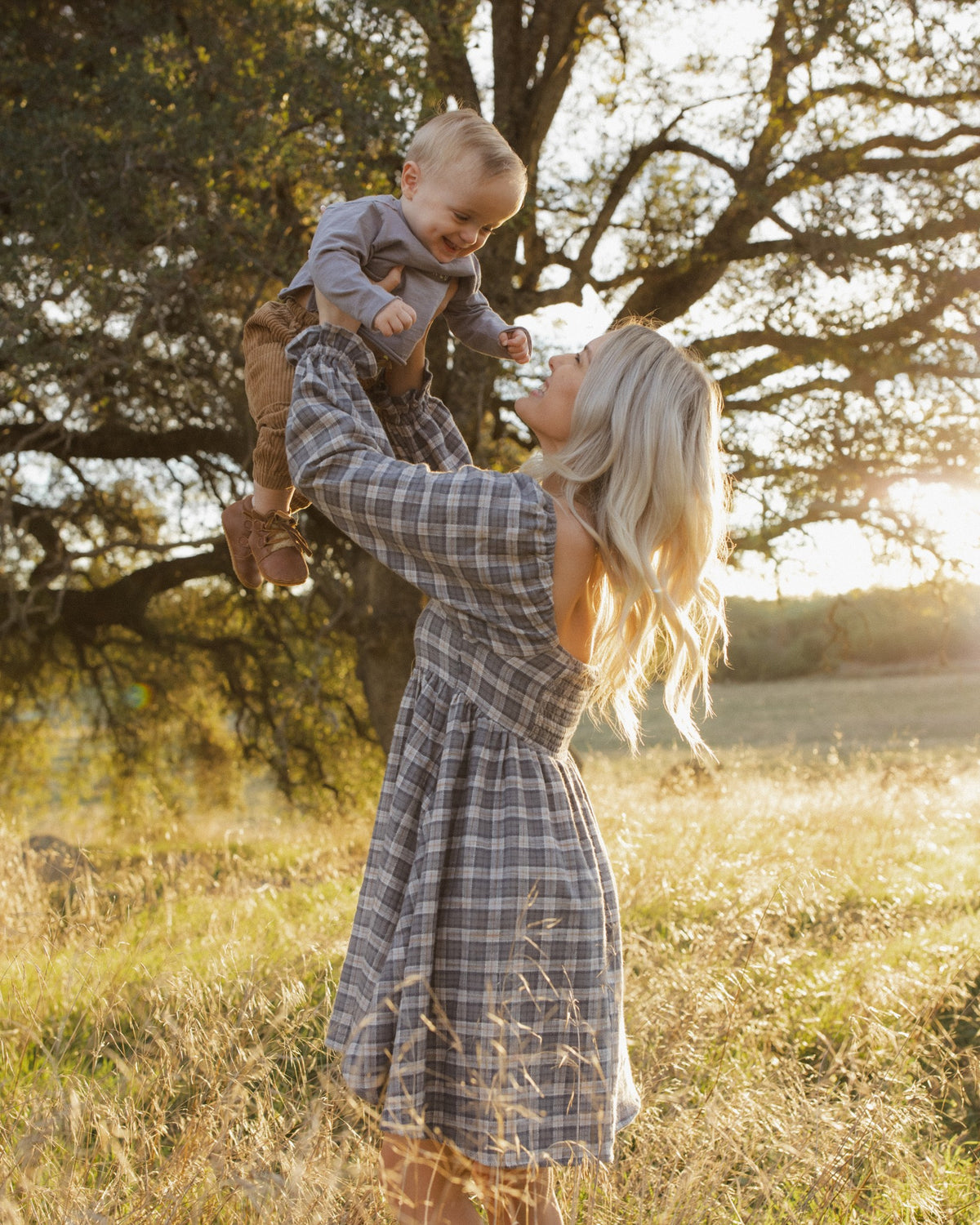 Mother lifting a baby wearing the Rylee + Cru Lucian pant in toffee in a sunlit field