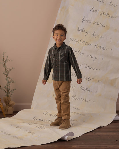 Boy standing on a handwritten backdrop wearing the Rylee + Cru pocketed flannel shirt in holiday plaid with tan pants