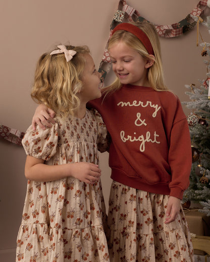 Two girls in holiday outfits, one in the Rylee + Cru Merry & Bright relaxed sweatshirt, standing in front of a Christmas tree
