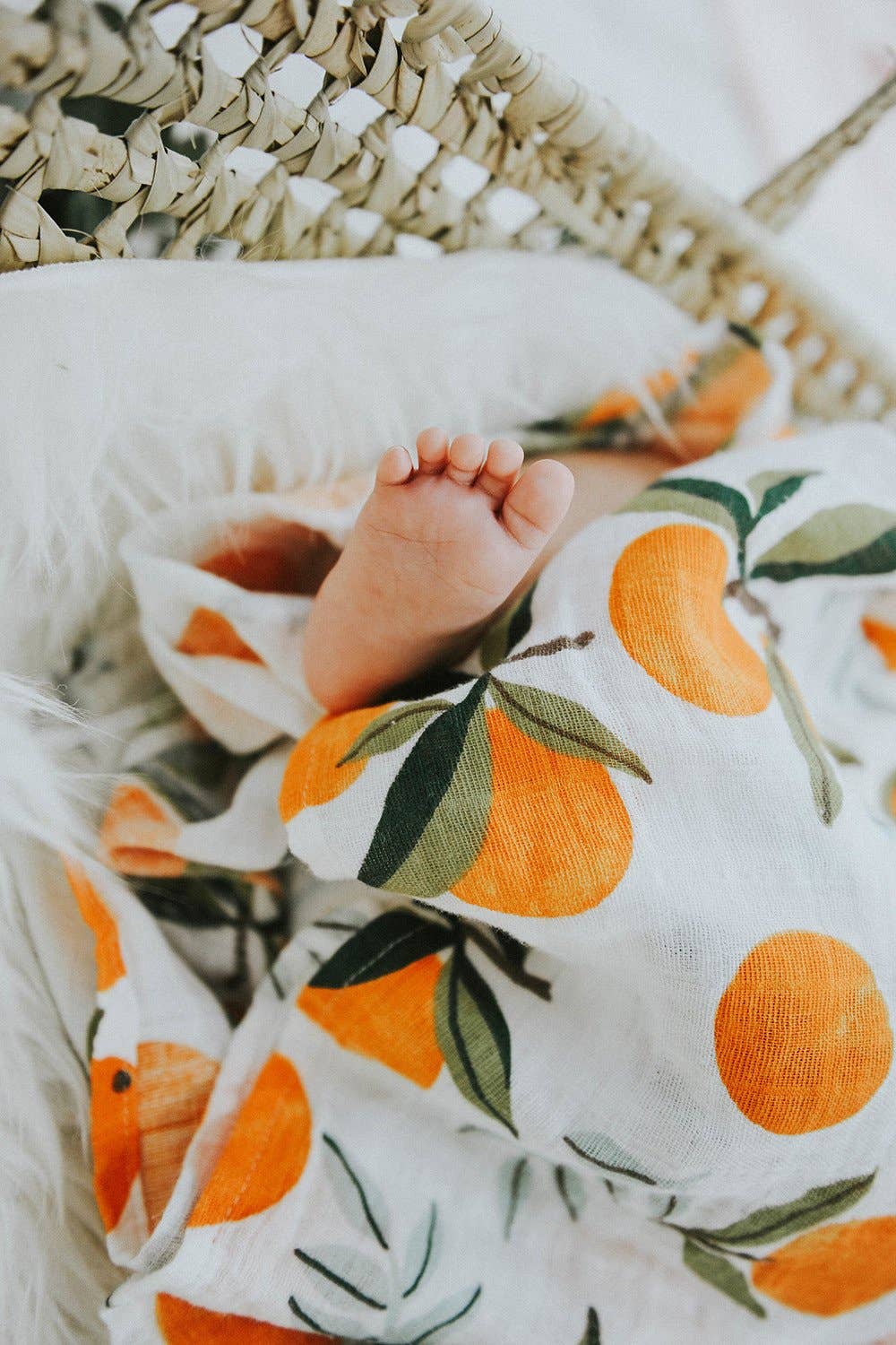 baby foot wrapped up in clementine swaddle. the oranges have green stems and leaves on them and are placed throughout either as a single clementine or in bunches of one or two clementines.