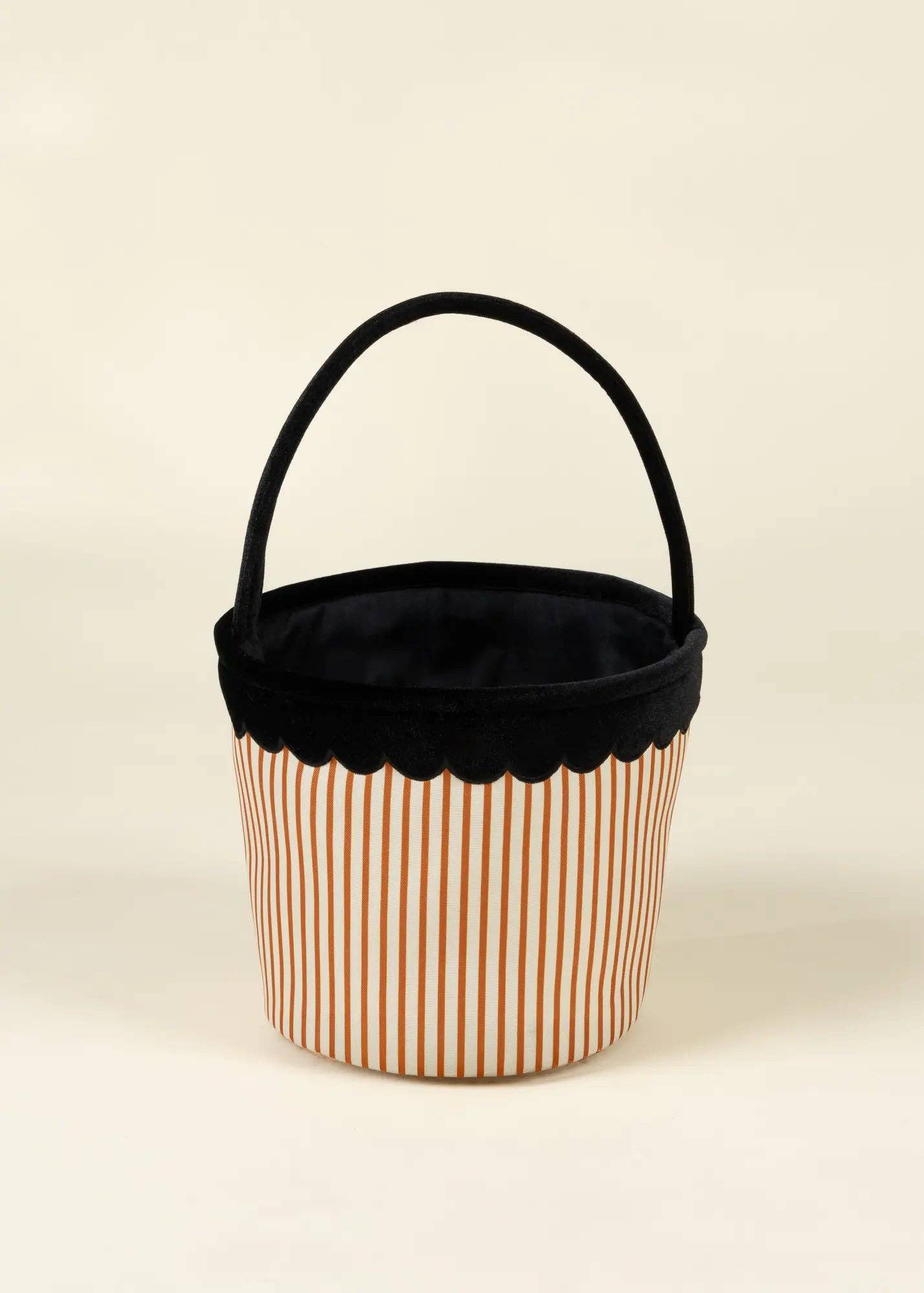 A small fabric storage basket with a black velvet handle and trim, featuring a white body with thin orange vertical stripes, set against a plain cream background.