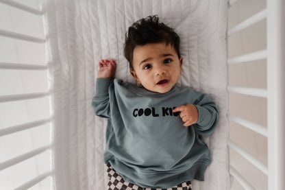 Boy laying down in crib wearing our Cool Kid sweatshirt. The back says "Cool Since Forever" Our bamboo terry is made with 66% Bamboo 28% Cotton and 5% Spandex. 