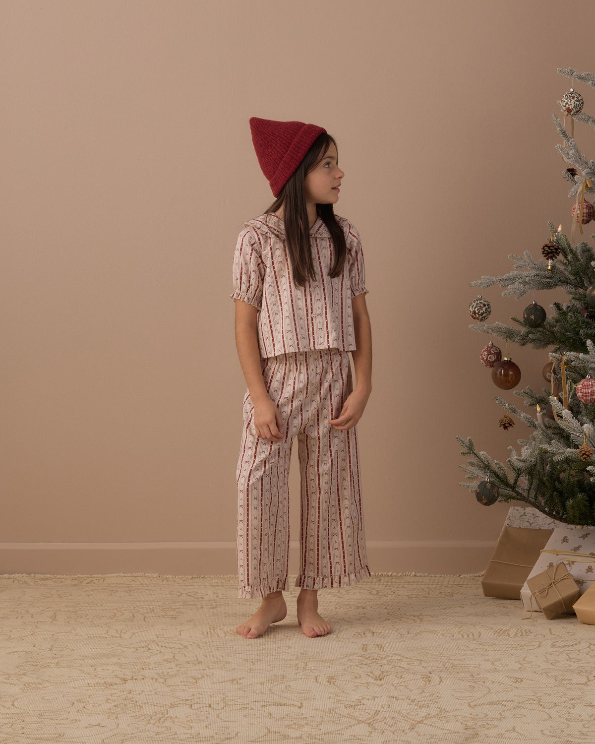 Girl looking to the side in the Rylee + Cru ruffle pajamas in candy cane lane beside a decorated Christmas tree