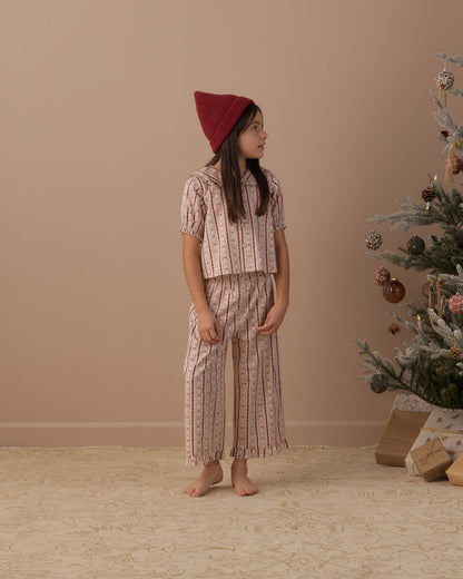 Girl looking to the side in the Rylee + Cru ruffle pajamas in candy cane lane beside a decorated Christmas tree