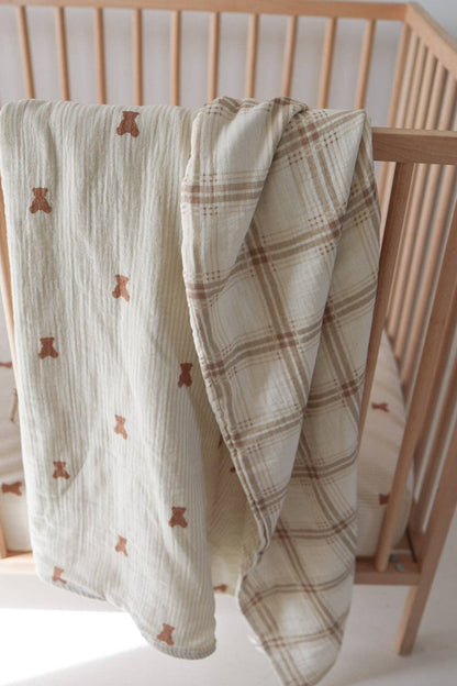 Forever French Baby Teddy and Ellis Plaid reversible muslin quilt draped over a wood crib, both sides visible