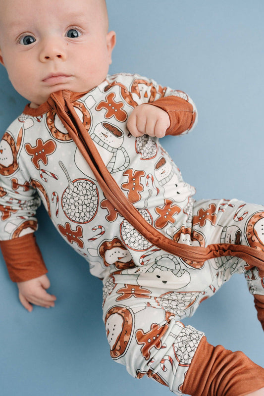 Baby wearing our hot cocoa bamboo sleeper. These hot cocoa pajamas feature gingerbread man cookies, hot chocolate, snowman and more Christmas cheer! Buttery soft, lightweight, breathable, and stretchy. Fold over mittens up to 12-18M. Fold over footies. 2-way zipper for easy diaper changes. 