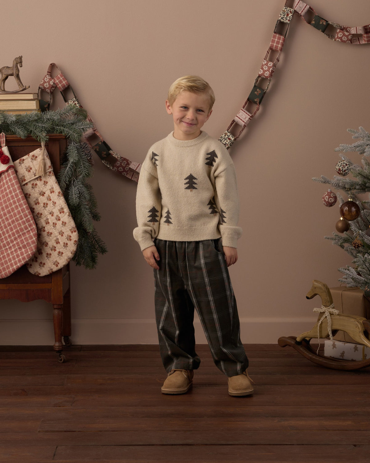 Boy in the Rylee + Cru Aspen sweater in tree jacquard with plaid pants standing in a holiday-decorated room