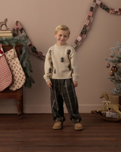 Boy in the Rylee + Cru Aspen sweater in tree jacquard with plaid pants standing in a holiday-decorated room