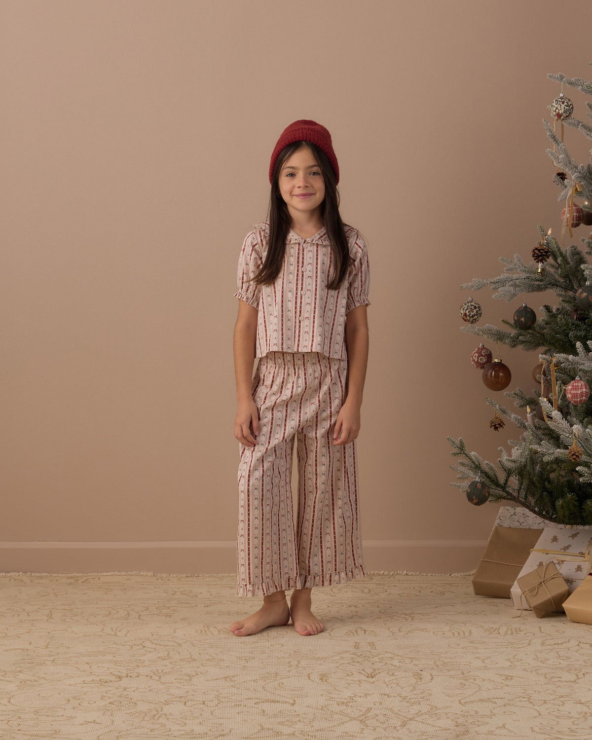 Girl standing with hands at her sides in the Rylee + Cru candy cane lane ruffle pajamas with a wrapped gift nearby