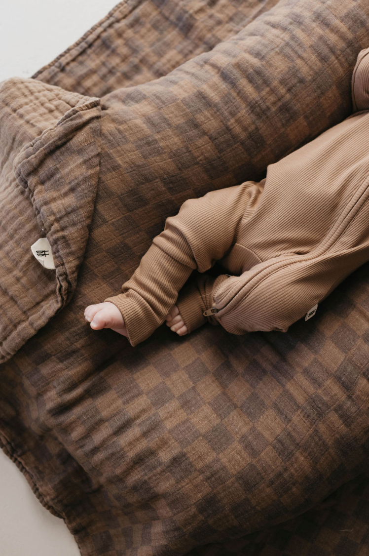 Baby in brown ribbed pants resting on the faded brown checkerboard muslin quilt