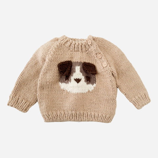 A tan-colored baby sweater featuring a knitted applique of a dog's face on the front, with three wooden buttons on the left shoulder.