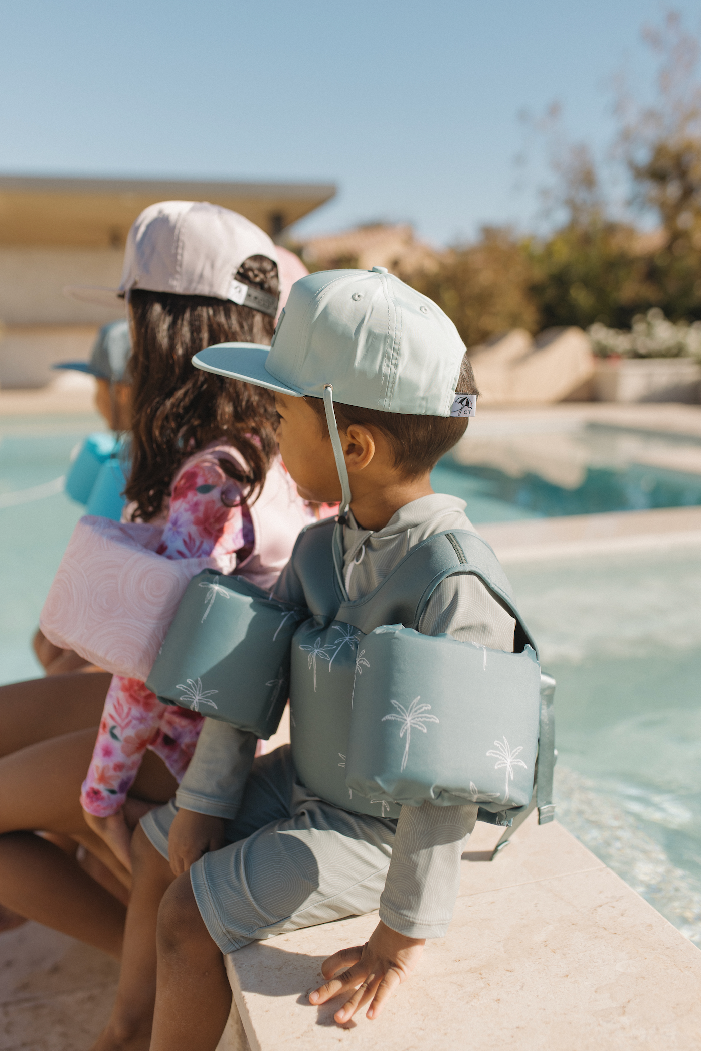Kids sitting on edge of pool wearing sea you on top floaties
