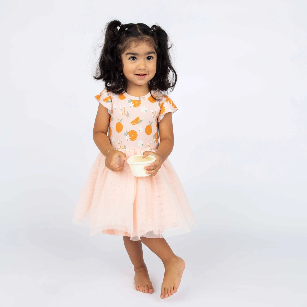 Girl wearing tulle twirl dress in freshly squeezed oranges pattern. 
