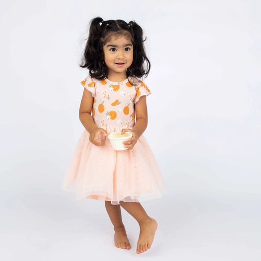 Girl wearing tulle twirl dress in freshly squeezed oranges pattern. 